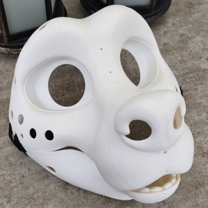 May include: White unpainted furry animal mask with large eye and nose holes. The mask has a textured surface and is made of a hard plastic material.