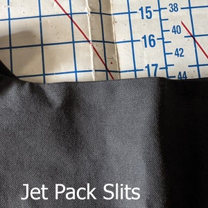 Peut inclure: Gros plan sur un tissu gris foncé avec deux fentes cousues dans le tissu. Le texte "Jet Pack Slits" est imprimé sous les fentes.
