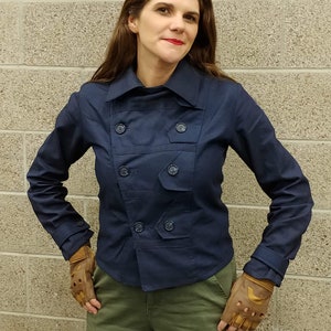 May include: A dark navy blue double-breasted jacket with a wide collar, long sleeves, and matching buttons, paired with olive green cargo pants featuring large side pockets and tan fingerless leather gloves with reinforced knuckle padding.