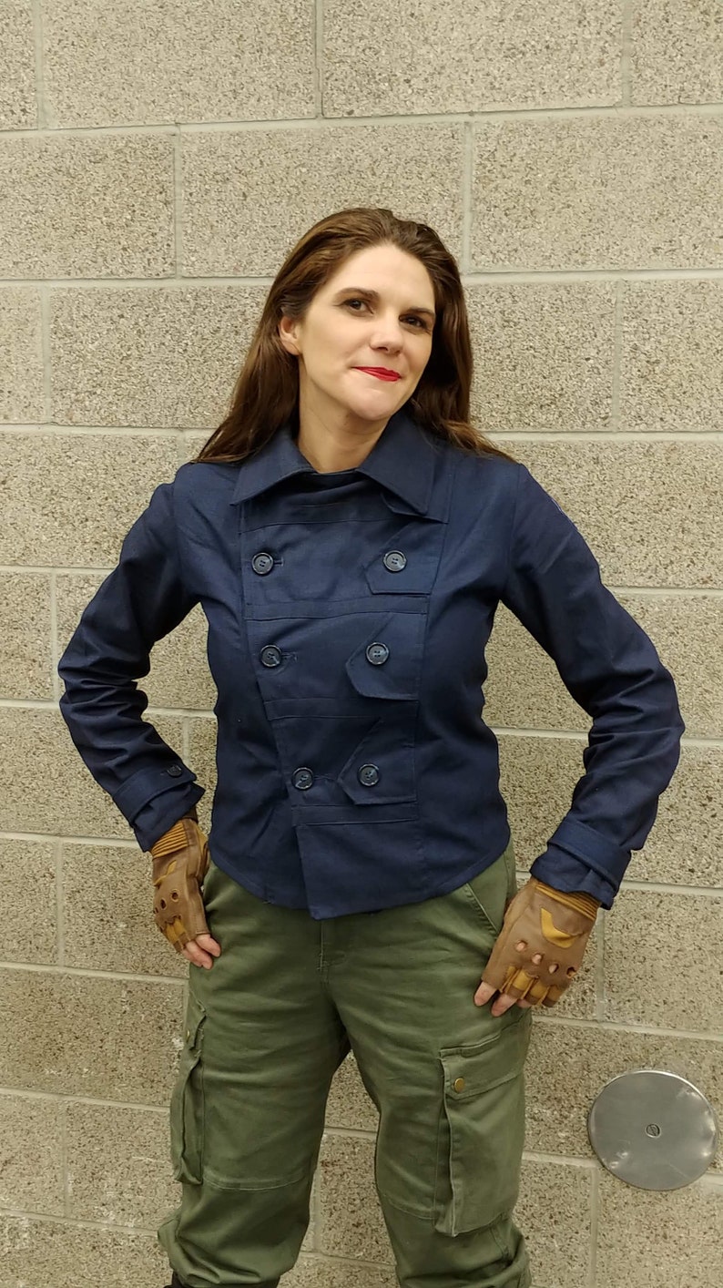 May include: A dark navy blue double-breasted jacket with a wide collar, long sleeves, and matching buttons, paired with olive green cargo pants featuring large side pockets and tan fingerless leather gloves with reinforced knuckle padding.