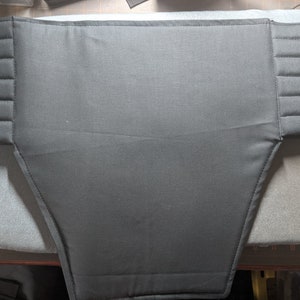 May include: A black fabric piece with a quilted design on the sides. The fabric is shaped like a large, upside-down triangle with rounded corners.