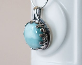 May include: A silver pendant with a light blue and white gemstone set in a decorative silver frame.