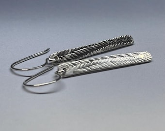 May include: A pair of silver earrings with a textured, braided design. The earrings are long and dangle.