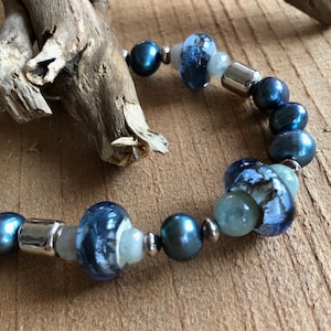 The aquamarine blue bracelet is an original design. The glass beads have shades of silver, blues from light to dark. The blue fresh water pearls measure about 6 mm and sterling silver accents. A sterling heart toggle finishes the 8 inch bracelet.