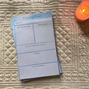 May include: A rectangular paper notepad titled Evening Reset with a light blue border. The page includes sections for Todays date, What went well today, What was hard, Did I ask for help, Gratitude, and Tomorrows Intention with blank writing spaces.