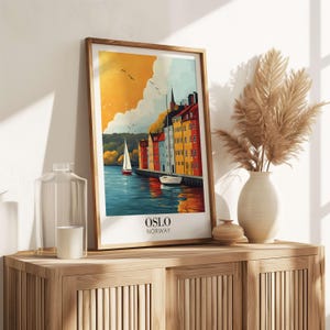 a framed poster of a scenic view of a harbor in Norway, with a sailboat and buildings in the background. The poster is displayed on a wooden shelf, accompanied by a vase of dried flowers and a glass jar.