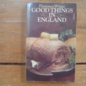 May include: A vintage cookbook titled "Good Things in England" by Florence White. The cover features a close-up of a savory dish with a butter garnish, set on a silver platter. The background is a warm, inviting brown.
