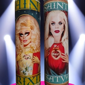 May include: Two glass prayer candles. One features a portrait of a person with blonde hair and the name "Trixie" at the bottom. The other candle has a portrait of a person with blonde hair and the name "Katya".