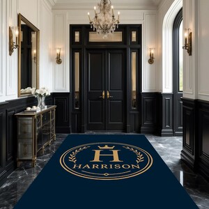 May include: A navy blue rectangular rug with a gold emblem featuring the letter "H" and the name "Harrison" in a formal font. The rug is in a grand entryway with black and white paneling, a chandelier, and a black door.
