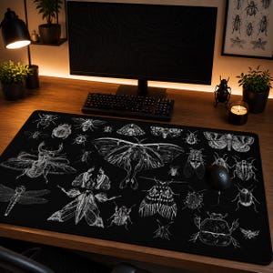 May include: A black rectangular desk mat featuring detailed white illustrations of various insects, including beetles, moths, and dragonflies. The mat is designed for use with a computer mouse and keyboard, providing a decorative and functional surface.