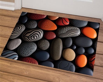 Può includere: Un tappetino per la porta con un design di pietre lisce e colorate in tonalità di nero, grigio, rosso, arancione e bianco. Le pietre sono disposte in modo casuale.