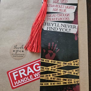 May include: A red bookmark with a black background and white text that reads "Blood Stains Are Red, Ultraviolet Lights Are Blue, I Read Enough Murderbooks, They'll Never Find You!" The bookmark has a red tassel and a yellow and black crime scene tape design. The text on the tape reads "Crime Scene - Do Not Cross".