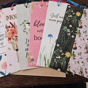 May include: A set of 8 colorful bookmarks with floral and botanical designs. The bookmarks feature various quotes, including "Happy Mother's Day", "Just one more page", and "Bloom with books".