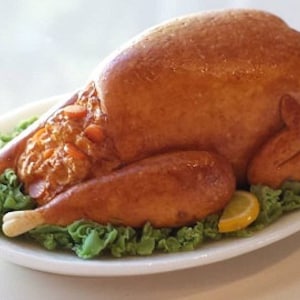 May include: A roasted turkey on a white platter with green lettuce and a lemon slice.