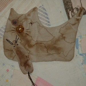 May include: A brown fabric cat with a bell and button sewn on its chest. The cat is holding a smaller brown fabric mouse in its paws.