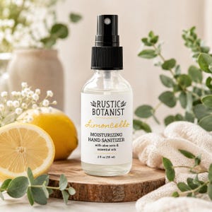 May include: A clear glass spray bottle of Rustic Botanist Limoncello moisturizing hand sanitizer with a black pump top. The white label features black text, yellow script, and a 2 fl oz (59 ml) volume indicator. The bottle contains aloe vera and essential oils.