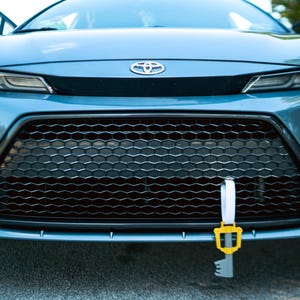 May include: A blue car with a black honeycomb grille and a yellow and white tow strap attached to the front bumper.