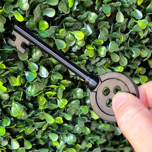 May include: A black key with a large, round button-shaped head. The key has a simple design with a single bow and a small, round hole in the head.