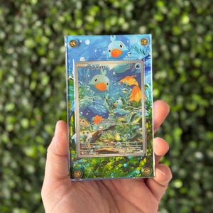 May include: A framed Pokémon trading card featuring a Ducklett illustration in a clear acrylic case. The card has a blue and green aquatic background with the text "Ducklett" and "Firefighting". The case is secured with gold-colored screws.