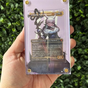 Puede incluir: Una carta coleccionable con el personaje Y'shtola, Night's Blessed, un Cat Warlock. La carta está en una funda protectora transparente con tornillos de esquina dorados. La ilustración de la carta representa a un personaje femenino con cabello blanco y un atuendo azul.
