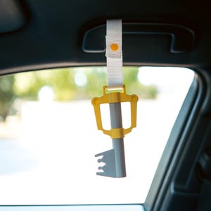 May include: A yellow and gray keyblade keychain hanging from the rearview mirror of a car.