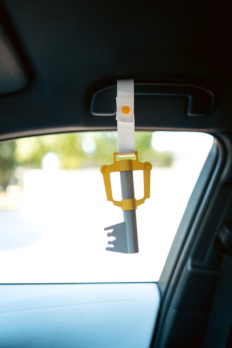 May include: A yellow and gray keyblade keychain hanging from the rearview mirror of a car.