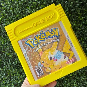 May include: A yellow Game Boy Color cartridge with a holographic image of Pikachu on the front. The game is titled "Pokémon Special Pikachu Edition" and has a "TM" symbol next to the title. The game is rated "E" for Everyone by the ESRB.