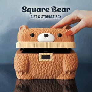 May include: A brown bear-shaped gift and storage box with the text "Square Bear" and "Gift & Storage Box". The box has a textured surface, black eyes, and a white nose. The lid is open, revealing a black interior.