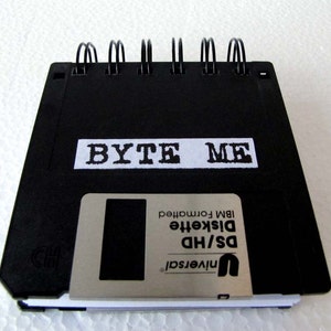 May include: A black notebook with a spiral binding. The front cover is a black floppy disk with the text "BYTE ME" printed in white on a white label. The floppy disk is labeled "Universal DS/HD Diskette IBM formatted".
