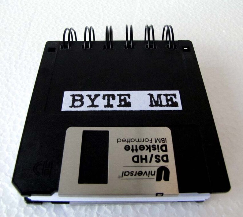 May include: A black notebook with a spiral binding. The front cover is a black floppy disk with the text "BYTE ME" printed in white on a white label. The floppy disk is labeled "Universal DS/HD Diskette IBM formatted".