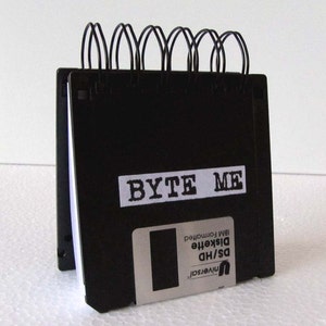 May include: A black notebook with a spiral binding made from stacked floppy disks. The notebook has a white label that says "BYTE ME".