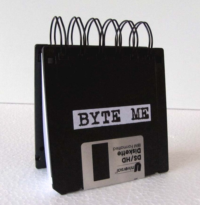 May include: A black notebook with a spiral binding made from stacked floppy disks. The notebook has a white label that says "BYTE ME".
