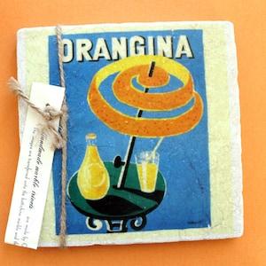 May include: A vintage-style coaster featuring a colorful illustration of an orange drink with the text "ORANGINA" in a bold, white font. The coaster is made of handmade marble and has a rustic, textured surface.