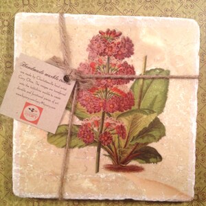 May include: Handmade marble coaster featuring a vintage botanical illustration of pink flowers with green leaves. The coaster is tied with twine and has a small tag with the text "Handmade marble coasters are made by Charlottesville local artist Cary Olive. The images are transferred onto the batichins marble to create durable and functional pieces of art. www.bycary.com/cary @bycarycom bycary".