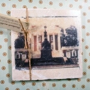 May include: A handmade marble coaster with a vintage photograph of a building with a white facade and a black roof. The text on the coaster reads "The images are transferred onto the battichian handmade marble trivets more information, please visit www.bbycary.co".