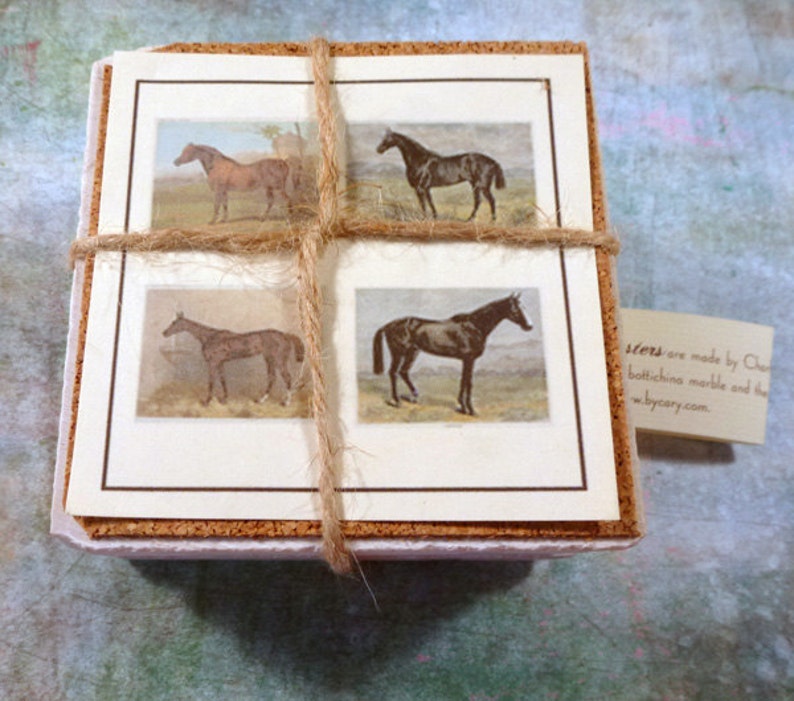 May include: Set of four cork-backed coasters featuring vintage illustrations of horses. The coasters are tied together with twine and have a brown border around each image. The text on the tag reads "Coasters are made by Cary using botticino marble and the finest materials. www.bycary.com."