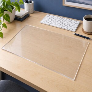 May include: A rectangular, clear acrylic desk mat with a smooth, transparent surface. The mat is designed to lay flat on a workspace, providing a protective layer for the desk surface while maintaining visibility of the wood grain underneath.