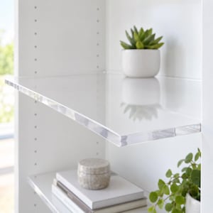 May include: A clear acrylic shelf installed within a white cabinet unit. The transparent shelf features a smooth, glossy surface and thick edges. A small white pot containing a green succulent sits on the shelf, reflecting on the surface.