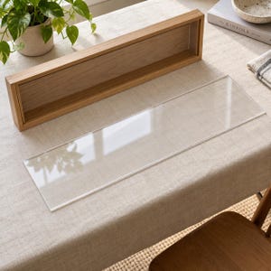 May include: A rectangular wooden shadow box frame with a light brown finish and a separate, clear, rectangular acrylic panel. The frame features a deep interior channel designed to hold the transparent acrylic sheet securely in place.