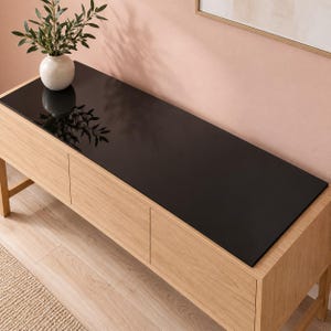 May include: A rectangular light oak wood console table featuring a smooth, solid black top surface. The piece includes two front-facing cabinet doors with a natural wood grain finish and stands on four sturdy legs, providing a clean, functional design.