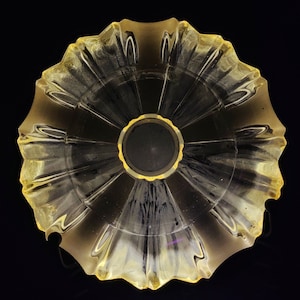 May include: A clear glass dish with a scalloped edge and a central design. The dish is yellow in colour and has a dark centre.