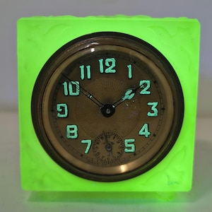 May include: A vintage square clock with a glowing green frame. The clock face is gold with black hands and luminous green numerals. The clock has a small seconds dial at the bottom and is marked "Made in France."