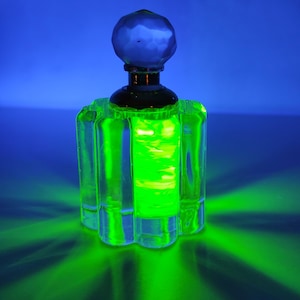 May include: A green glass bottle with a clear glass stopper. The bottle is illuminated with a green light, creating a glowing effect.