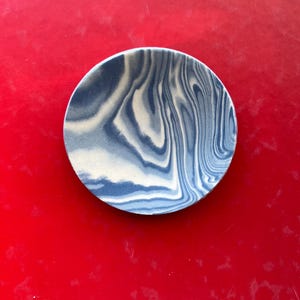 Könnte beinhalten: Eine kleine, runde, weiße und blaue marmorierte Keramikschale. Die Schale hat ein wirbelndes Muster aus Blau und Weiß.
