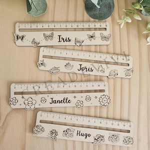 Può includere: Righelli in legno con disegni tagliati al laser e nomi: Iris, Joris, Janelle e Hugo. Ogni righello misura 15 cm di lunghezza e presenta elementi decorativi come farfalle, veicoli e fiori. Ideale per bambini.