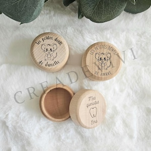 Könnte beinhalten: Zahnaufbewahrungsboxen aus Holz mit eingravierten Designs. Eine Box zeigt eine Mausillustration und den Text "Les petites dents de Janelle". Eine andere Box hat den Text "Les petites dents de Ambre". Eine dritte Box hat den Text "Mes quenottes Ema".
