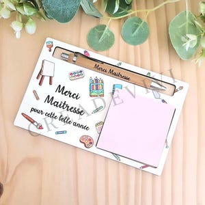 Könnte beinhalten: Ein weißer Schreibtisch-Organizer mit Stift, Notizblock und Illustrationen von Kunstbedarf. Der Stift ist mit "Merci Maitresse" graviert. Der Organizer trägt die Worte "Merci Maitresse pour cette belle année" und farbenfrohe Illustrationen.