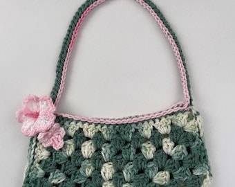 May include: A small green and white crocheted handbag with a pink crocheted flower accent. The bag has a pink and green crocheted strap.