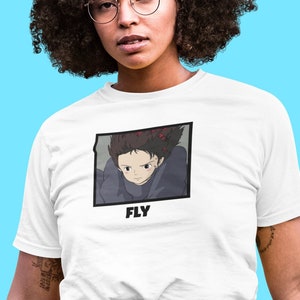Könnte beinhalten: Weißes T-Shirt mit einem gerahmten Anime-Motiv einer Person mit dunklen Haaren und dem Wort "FLY". Das T-Shirt wird von einer Person mit lockigem, dunklem Haar, Brille und Jeans vor hellblauem Hintergrund getragen.