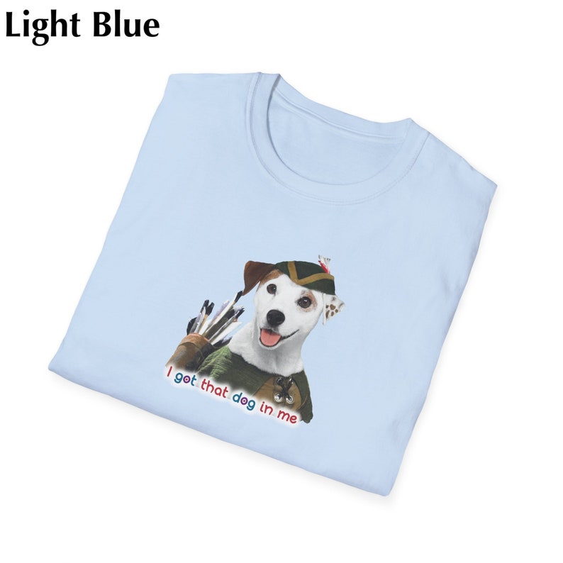 May include: Light blue t-shirt featuring a cartoon dog dressed as Robin Hood, with a quiver of arrows. The text "I got that dog in me" is printed below the dog in red, white, and blue. The shirt is folded.